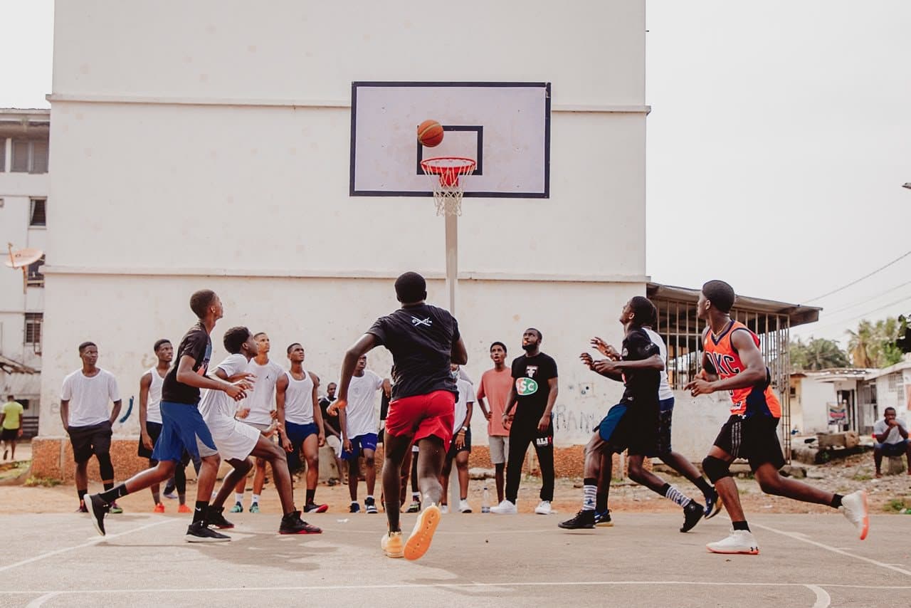 Match sur un playground : un joueur tire sous le panier, les autres suivent l'action