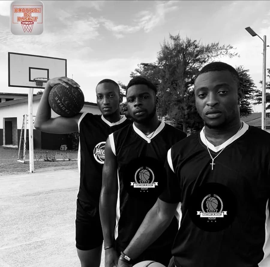 Trois joueurs en maillots noirs, ballon en main, sur un terrain